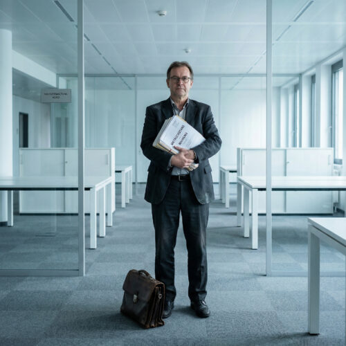 In einem leeren Großraumbüro hält ein Vertreter einen dicken Stapel unbezahlter Mietrechnungen in den Händen.