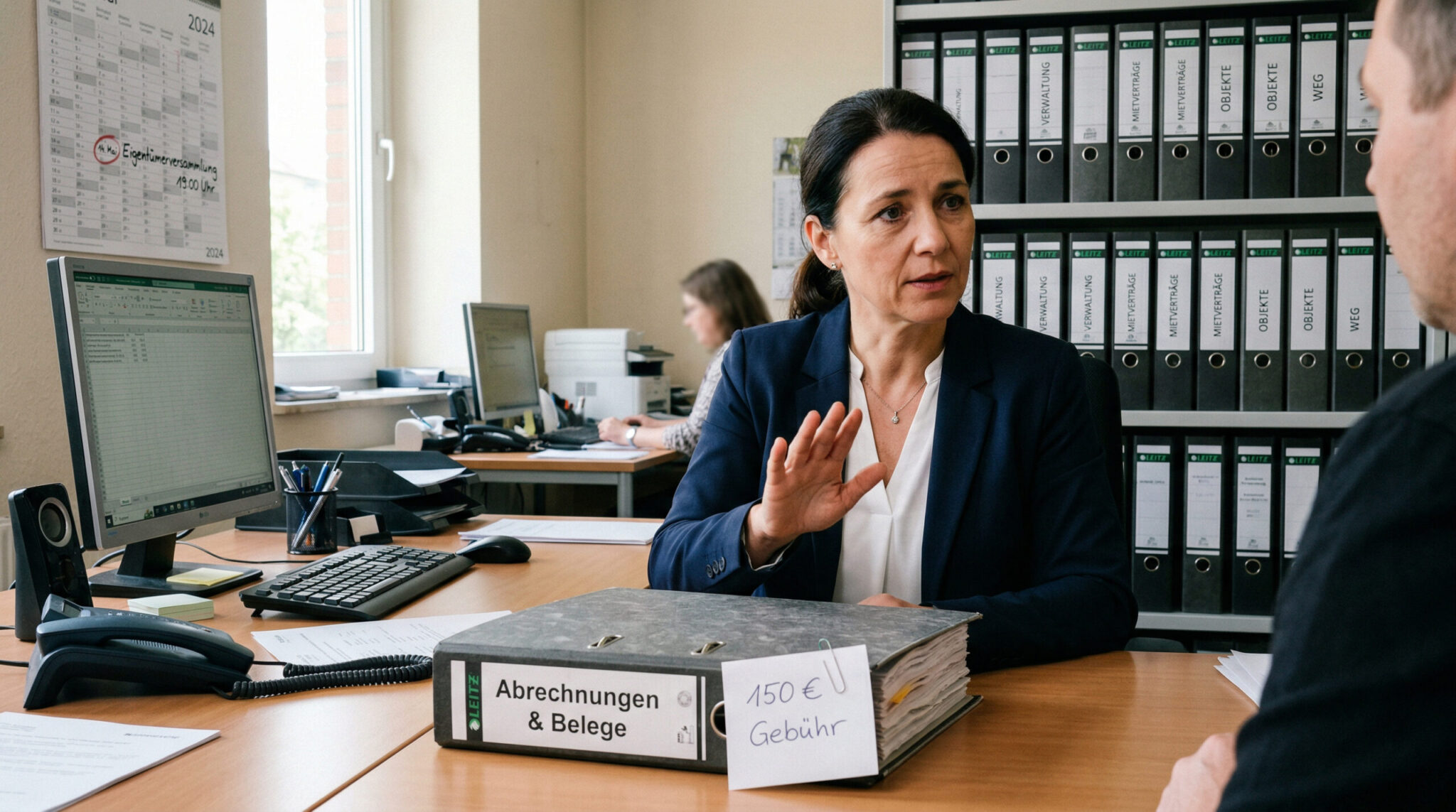 Aktenordner mit Gebühren-Zettel in einer Hausverwaltung, im Hintergrund ein Kalender mit Termin Eigentümerversammlung.